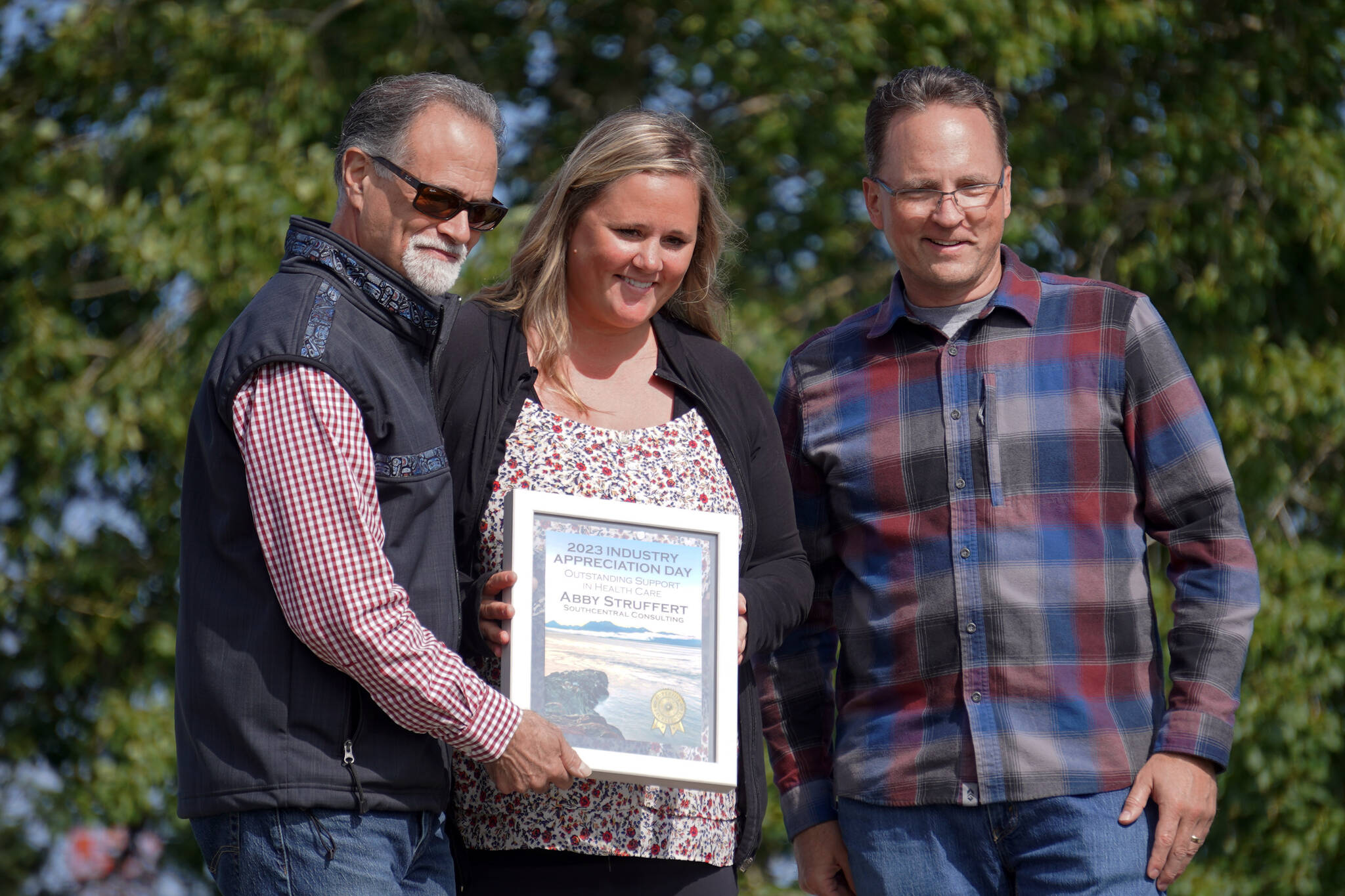 Abby Struffert of Southcentral Consulting, center, receives the Outstanding Support in Health Care Award from Kenai Peninsula Borough Mayor Peter Micciche and Rep. Ben Carpenter, R-Nikiski, during Industry Appreciation Day festivities at the Kenai softball greenstrip on Saturday, Aug. 19, 2023. (Jake Dye/Peninsula Clarion)