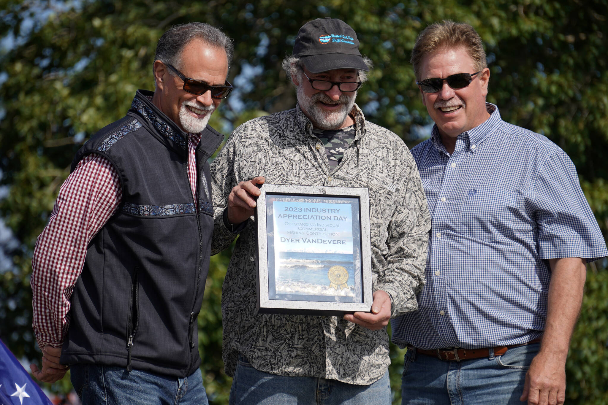 Dyer VanDevere, center, receives the Outstanding Individual Commercial Fishing Contribution Award from Kenai Peninsula Borough Mayor Peter Micciche and City of Kenai Mayor Brian Gabriel during Industry Appreciation Day festivities at the Kenai softball greenstrip on Saturday, Aug. 19, 2023. (Jake Dye/Peninsula Clarion)