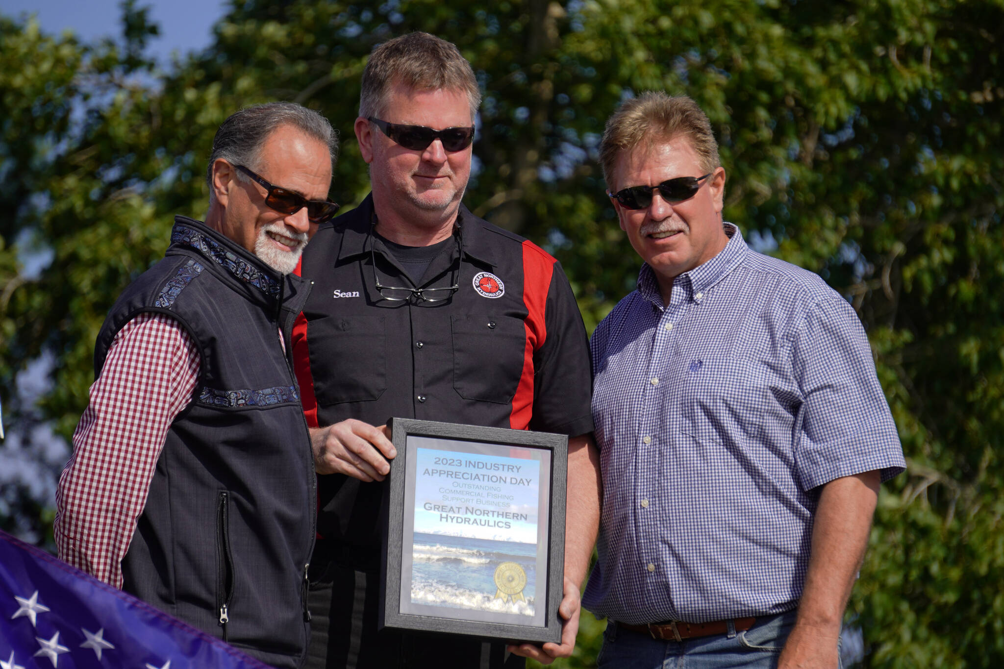 Sean Harwager, center, receives the Outstanding Commercial Fishing Support Business Award for his Great Northern Hydraulics from Kenai Peninsula Borough Mayor Peter Micciche and City of Kenai Mayor Brian Gabriel during Industry Appreciation Day festivities at the Kenai softball greenstrip on Saturday, Aug. 19, 2023. (Jake Dye/Peninsula Clarion)