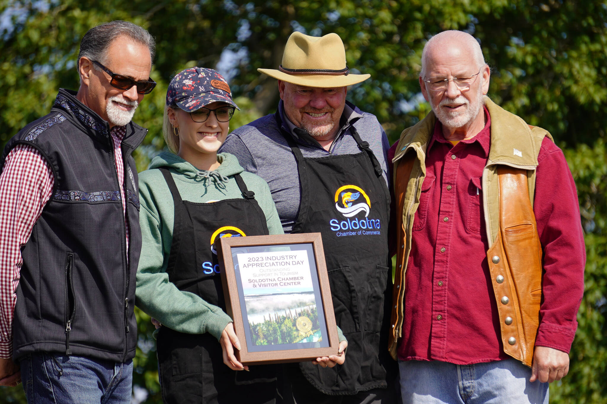 Soldotna Chamber of Commerce and Visitor Center Executive Director Maddy McElrea and Board President Jerry Herring, center, receive the Outstanding Support in Tourism Award from Kenai Peninsula Borough Mayor Peter Micciche and Soldotna Mayor Paul Whitney during Industry Appreciation Day festivities at the Kenai softball greenstrip on Saturday, Aug. 19, 2023. (Jake Dye/Peninsula Clarion)