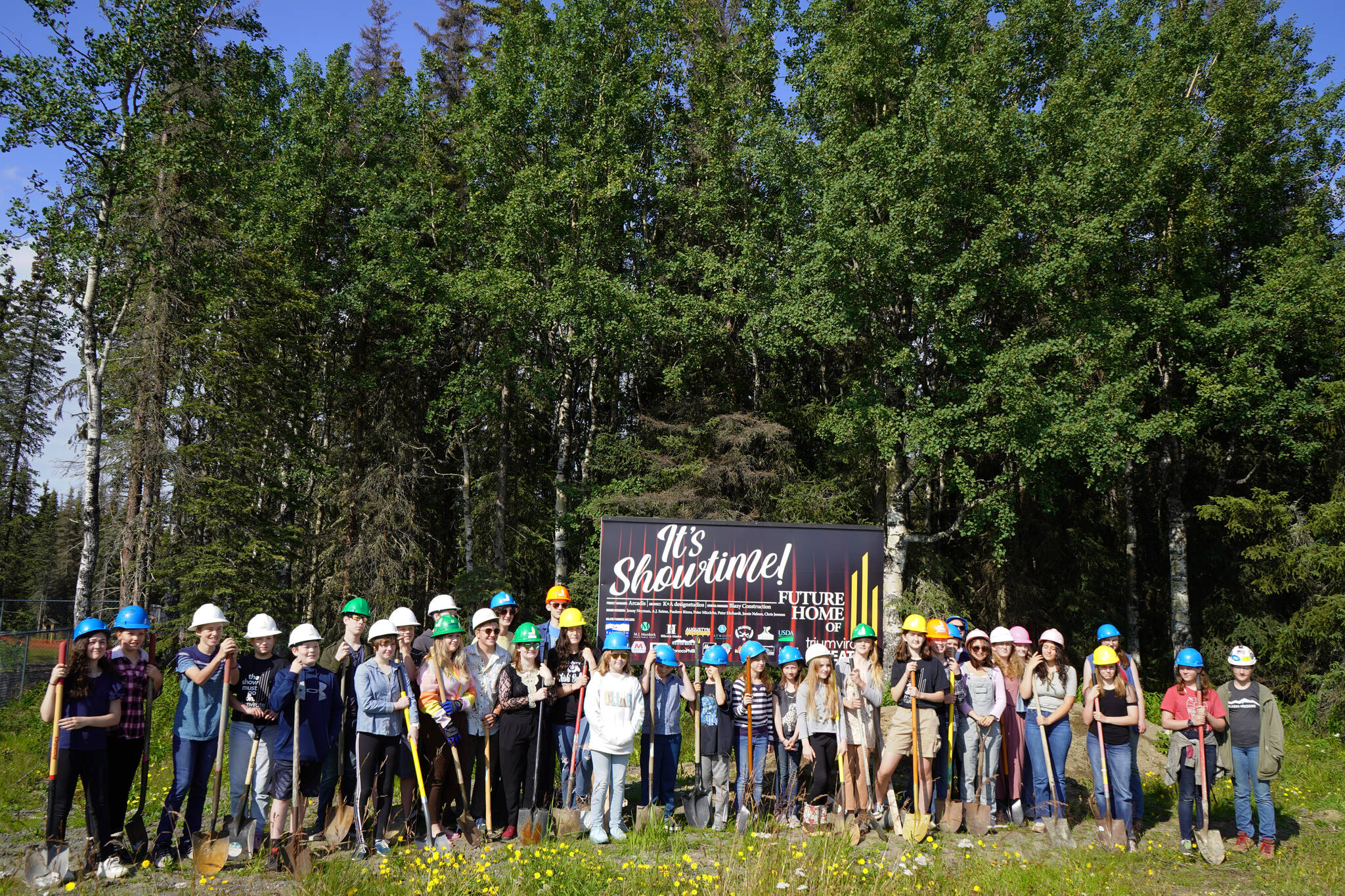 More than 30 assembled Triumvirate Theater performers stand together before the ceremonial groundbreaking at the future home of Triumvirate Theatre in Kenai, Alaska, on Saturday, Aug. 19, 2023. (Jake Dye/Peninsula Clarion)
