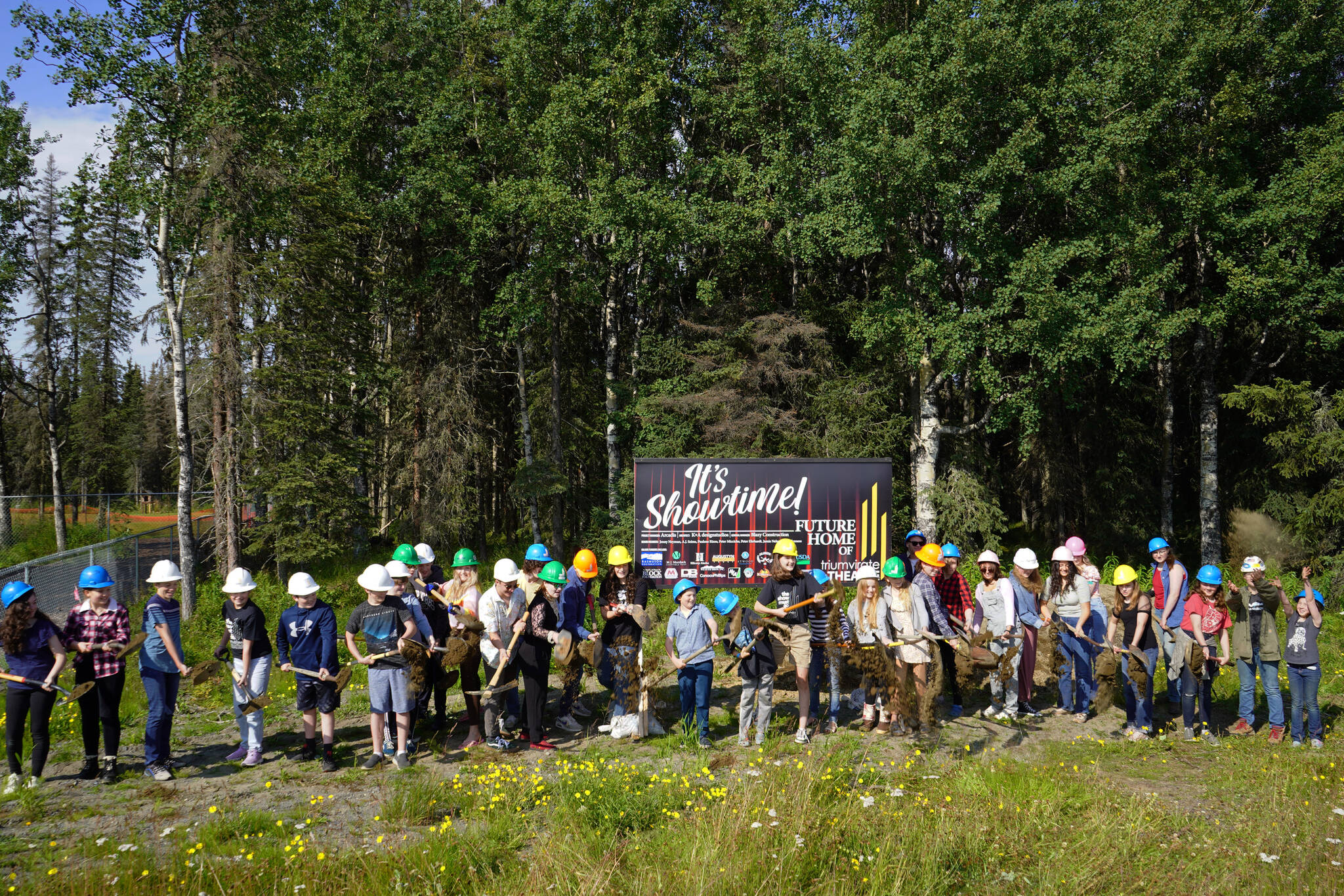 More than 30 assembled Triumvirate Theatre performers toss dirt in the air at the conclusion of a ceremonial groundbreaking at the future home of Triumvirate Theatre in Kenai, Alaska, on Saturday, Aug. 19, 2023. (Jake Dye/Peninsula Clarion)