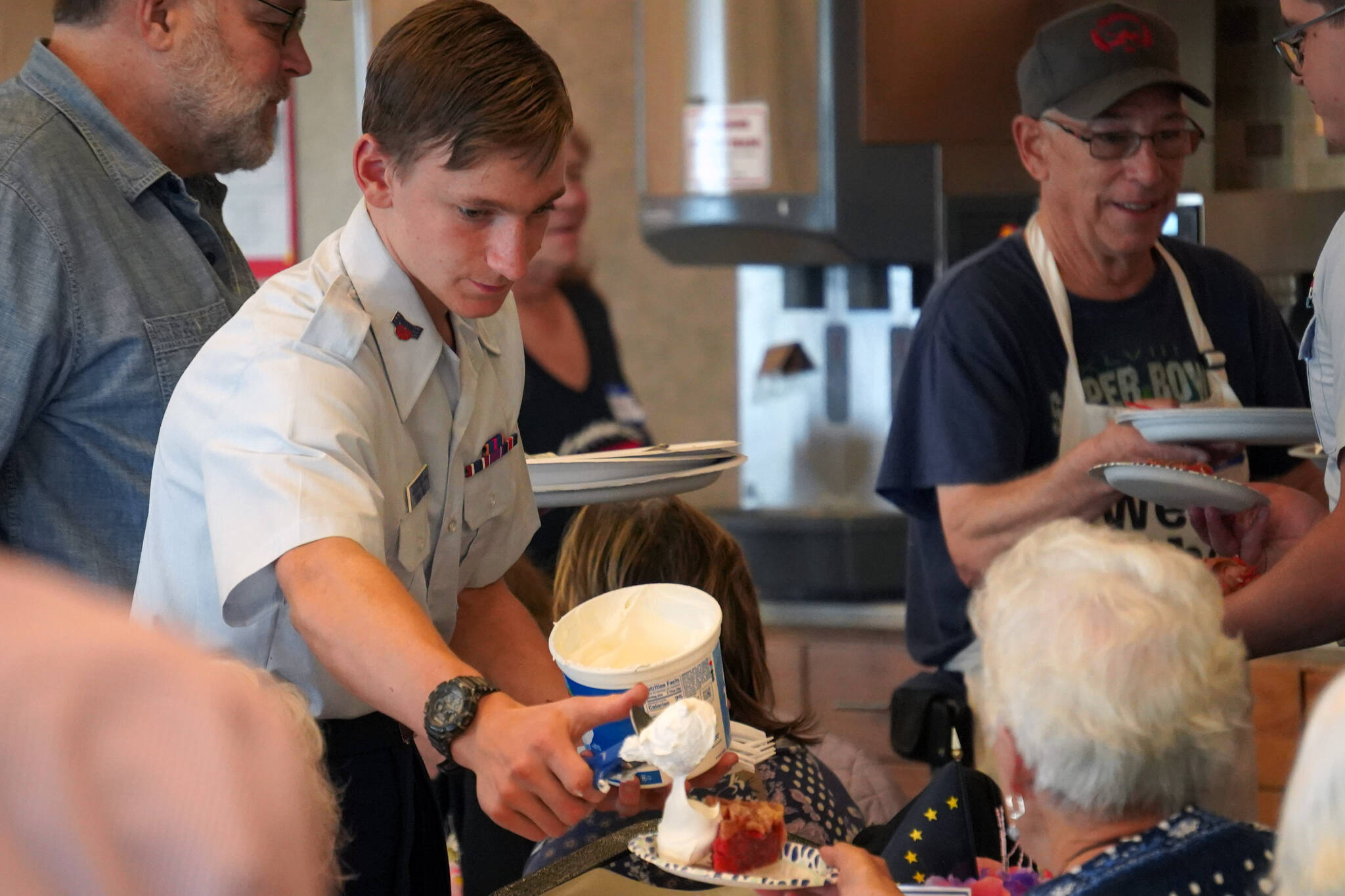 A Civil Air Patrol cadet administers a hearty dollop of Cool Whip to a slice of pie at the Old Timer’s Luncheon at the Kenai Senior Center in Kenai, Alaska, on Thursday, Aug. 31, 2023. (Jake Dye/Peninsula Clarion)