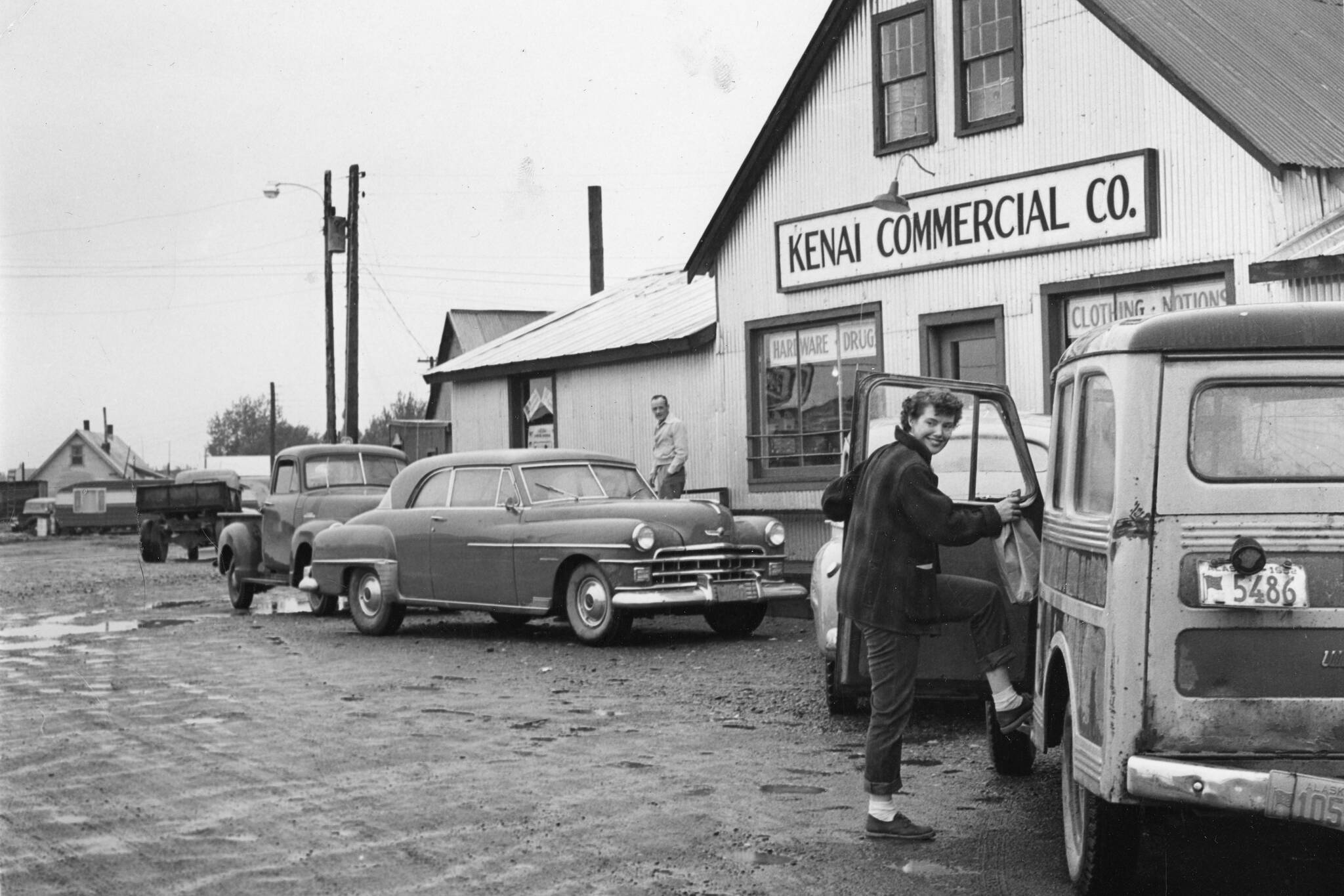 [1a—] After doing business in the Kenai Commercial Company store, Rusty Lancashire climbs into family station wagon, with its sagging back bumper, to head for home. (1954 photo by Bob and Ira Spring for Better Homes & Garden magazine)