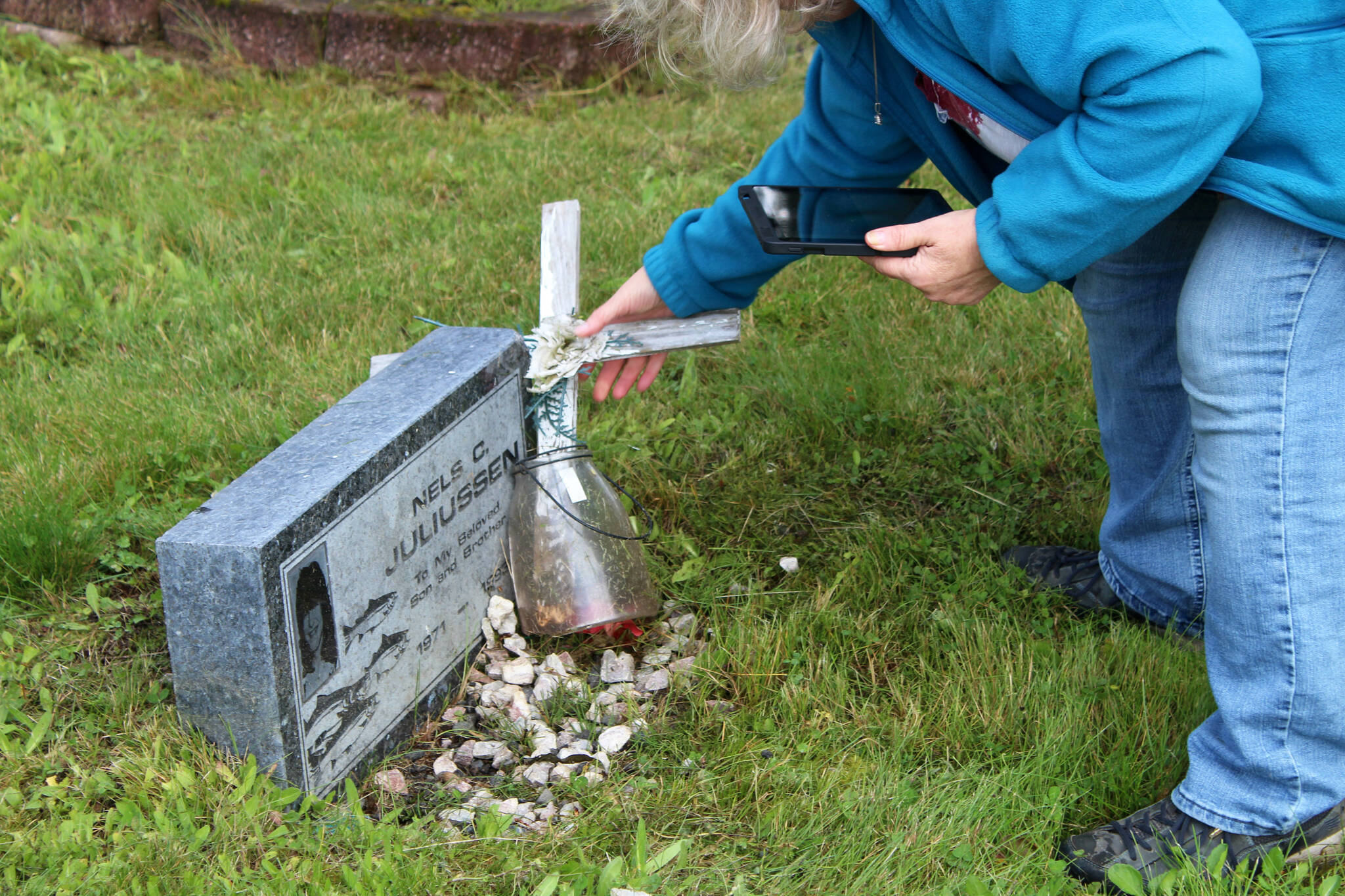 Victoria Askin rights a cross at the headstone of Nels C. Juliussen in the Kenai Cemetery as part of a city imaging project on Friday, Sept. 8, 2023, in Kenai, Alaska. (Ashlyn O’Hara/Peninsula Clarion)