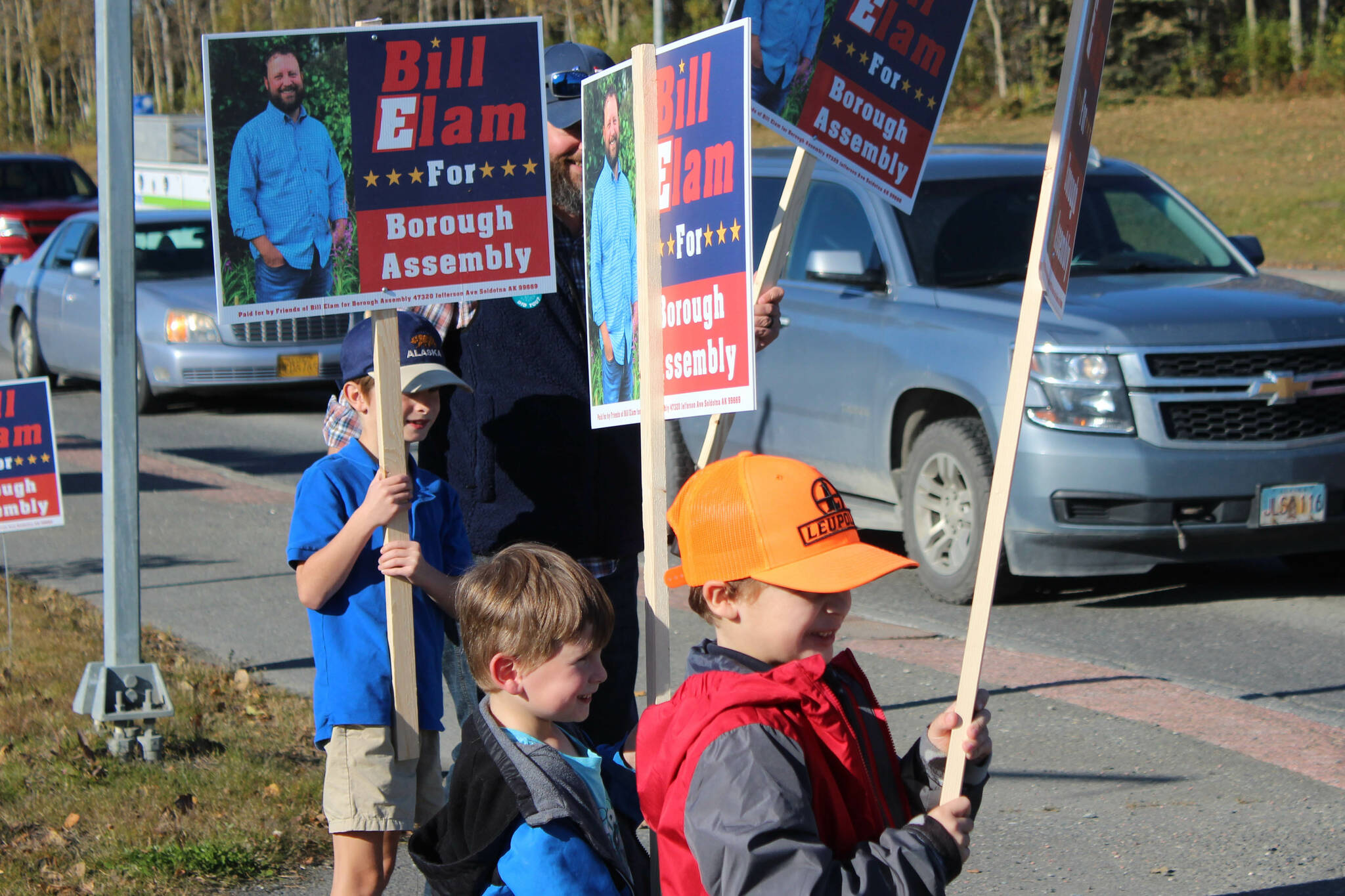 From left: William, Andrew and James Elam wave signs for their dad, Kenai Peninsula Borough Assembly candidate Bill Elam, on election day on Tuesday, Oct. 3, 2023, in Soldotna, Alaska. (Ashlyn O’Hara/Peninsula Clarion)