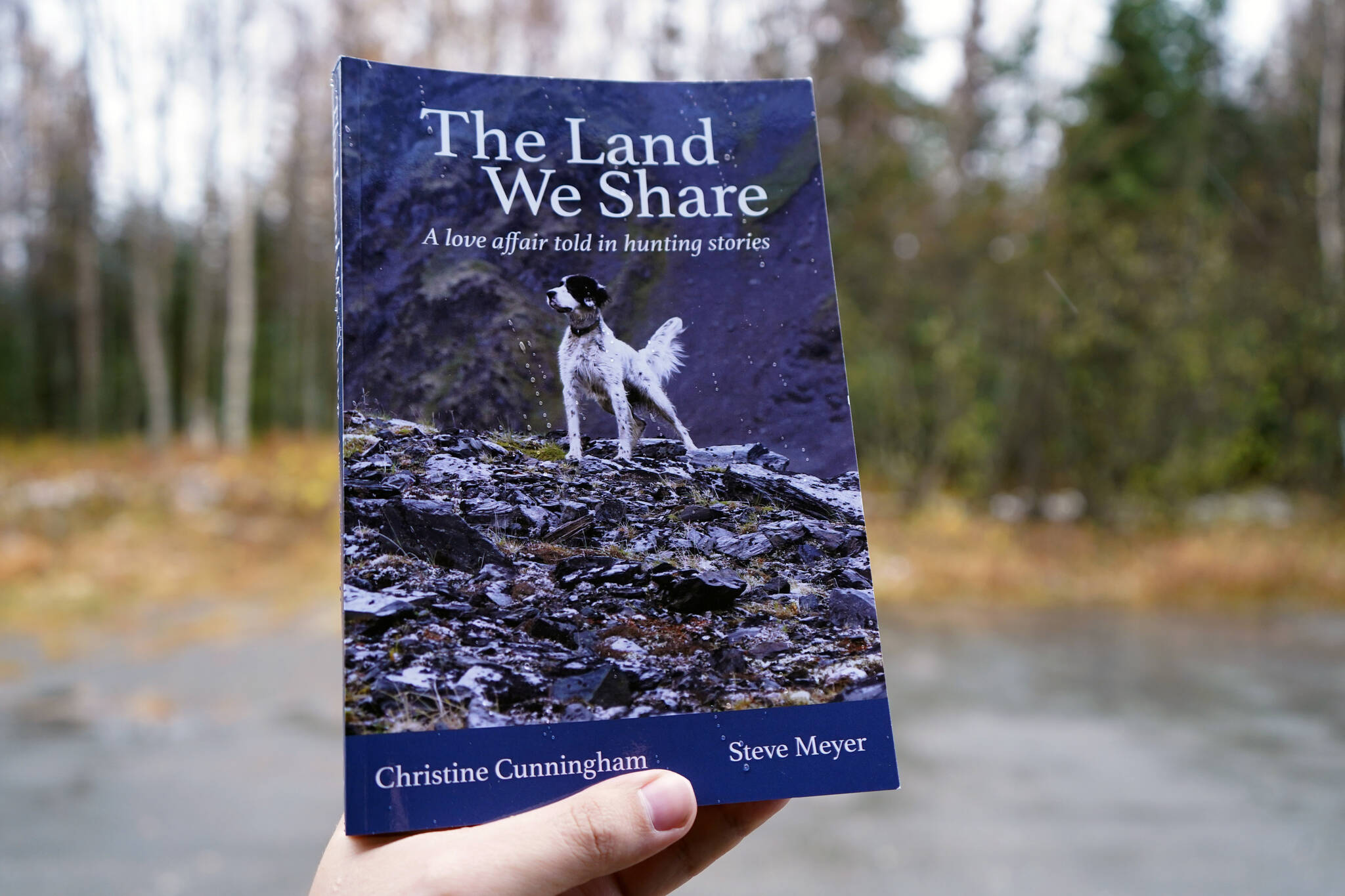 Jake Dye/Peninsula Clarion
“The Land We Share: A Love Affair Told in Hunting Stories” is held aloft under light rainfall in Kenai Thursday.