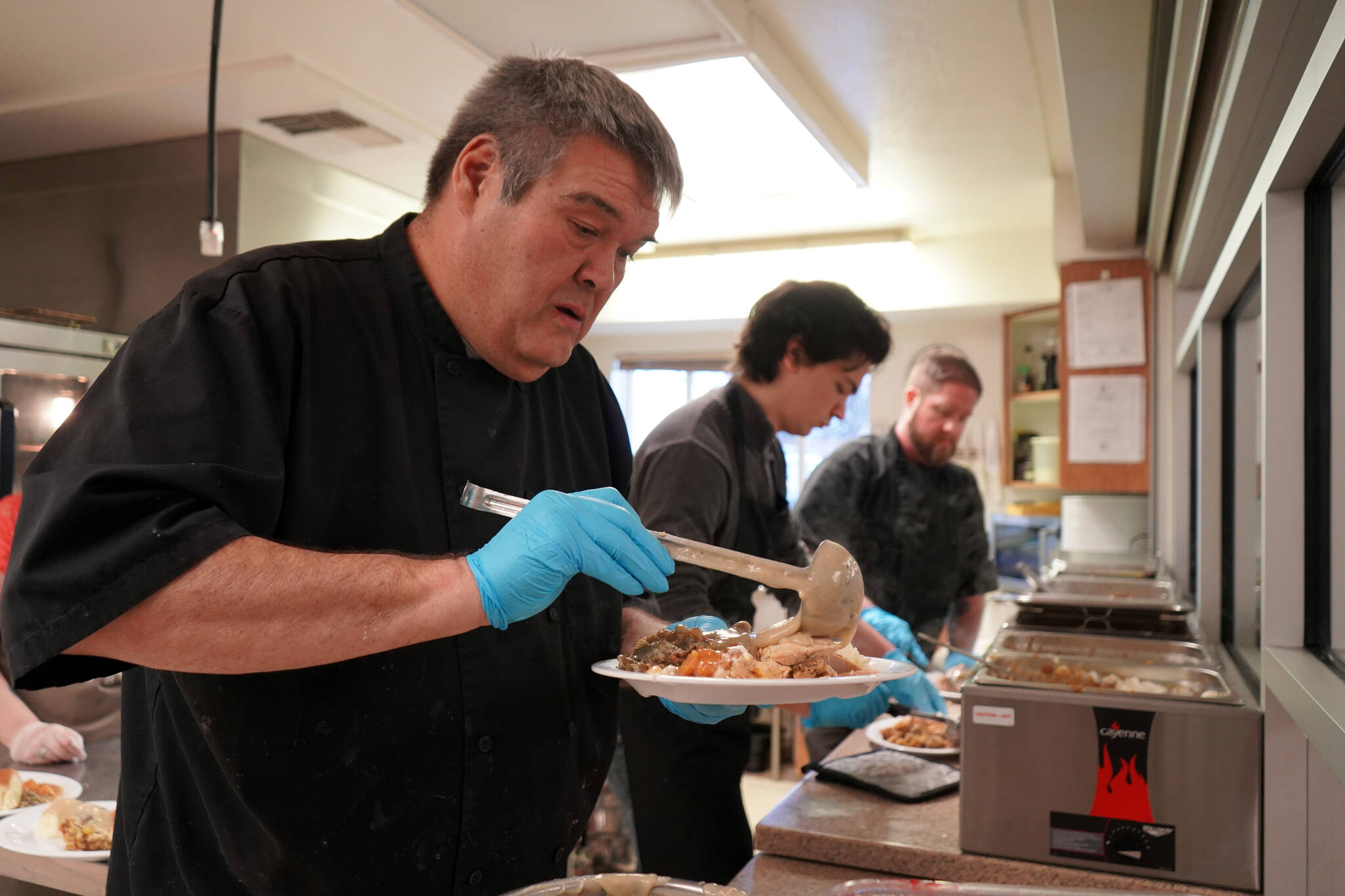 Mark Keel, Coltin Yancey and Chef Stephen Lamm plate and serve the Thanksgiving meal at the Kenai Peninsula Food Bank in Soldotna, Alaska, on Wednesday, Nov. 22, 2023. (Jake Dye/Peninsula Clarion)