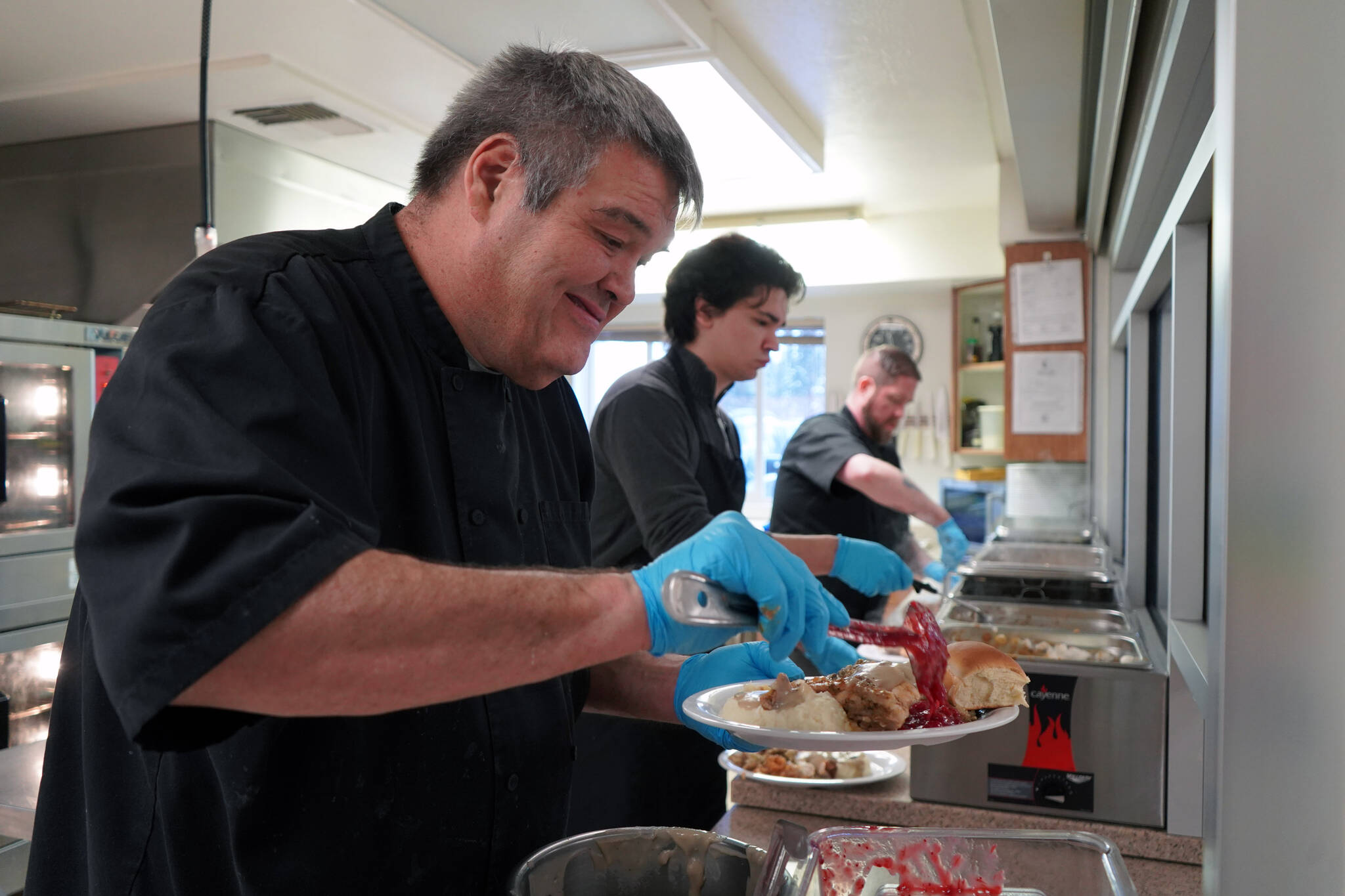 Mark Keel, Coltin Yancey and Chef Stephen Lamm plate and serve the Thanksgiving meal at the Kenai Peninsula Food Bank in Soldotna, Alaska, on Wednesday, Nov. 22, 2023. (Jake Dye/Peninsula Clarion)