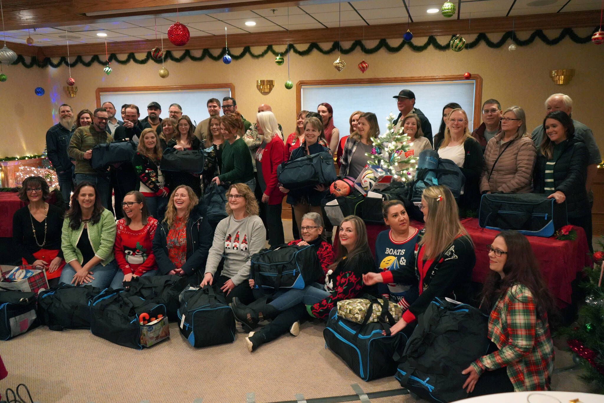 The Kenai Peninsula Association of Realtors sits with duffel bags of Christmas gifts donated to the Kenai Peninsula Borough School District’s Students in Transition program at Kenai Catering in Kenai, Alaska, on Thursday, Dec. 14, 2023. (Jake Dye/Peninsula Clarion)