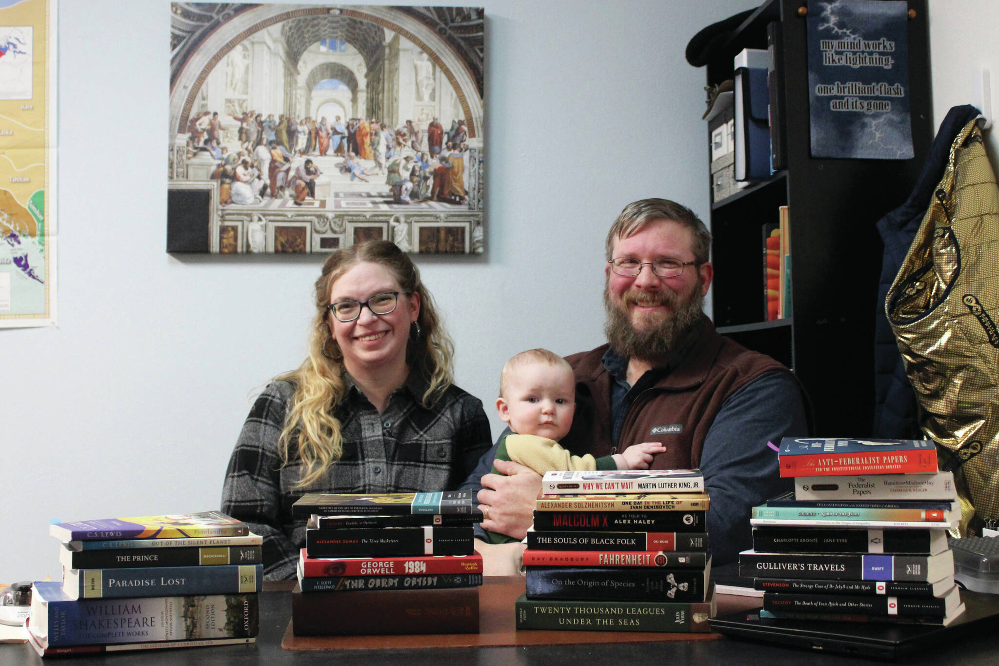 From left: Kylie Wilcox, Bernard Wilcox and Milton Wilcox sit behind the books Milton teaches as humanities at Kenai Classical School on Wednesday in Kenai. Kylie’s New Year’s resolution for 2024 is to read all of the book’s on Milton’s high school syllabus. (Ashlyn O’Hara/Peninsula Clarion)