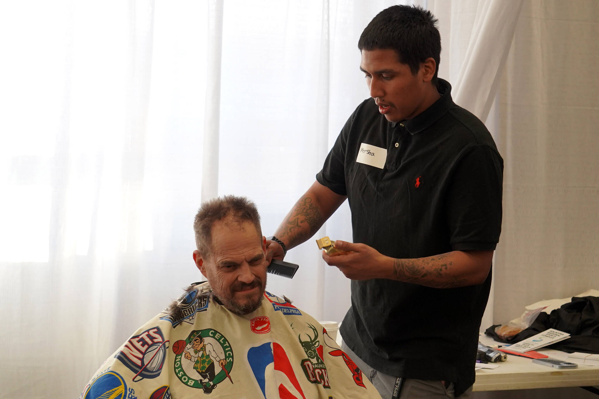 Mersha Tamrat, right, gives free haircuts to attendees at the 13th Annual Project Homeless Connect at the Soldotna Regional Sports Complex in Soldotna, Alaska, on Tuesday, Jan. 30, 2024. (Jake Dye/Peninsula Clarion)