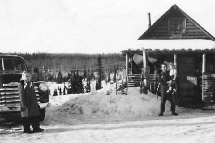 Floyd “Pappy” Keeler, standing in 1951 in front of his cabin on the homestead of his son Jack, is holding a girl who is likely Barbara Sandstrom, while her sister Rhoda, standing by a truck, looks on. Ray Sandstrom photo courtesy of the KPC historical photo archive.