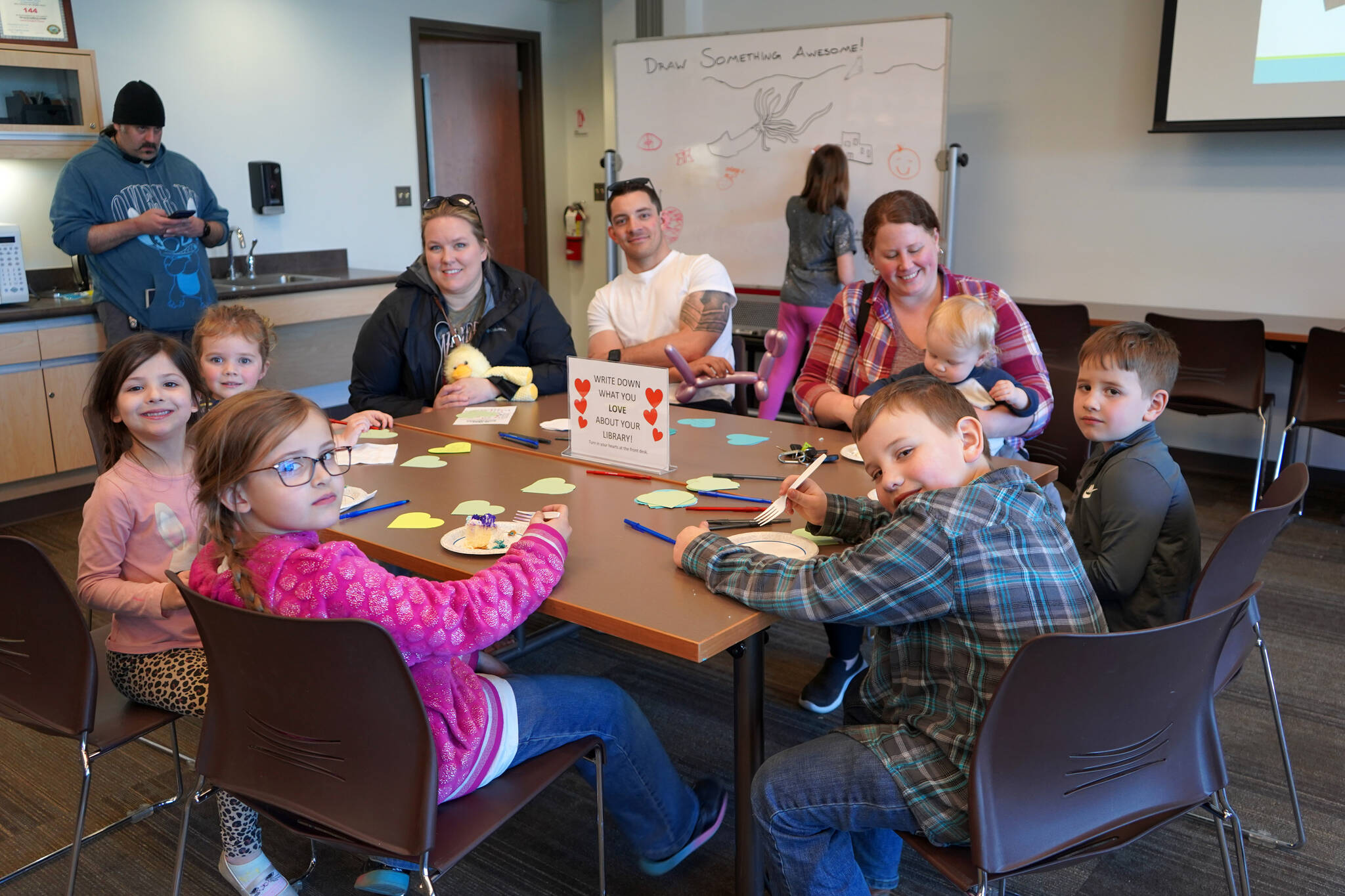 Children and families gather around a table to eat cake and write down what they love about their library at a 10th anniversary celebration for the expansion of the Soldotna Public Library in Soldotna, Alaska, on Monday, April 29, 2024. (Jake Dye/Peninsula Clarion)
