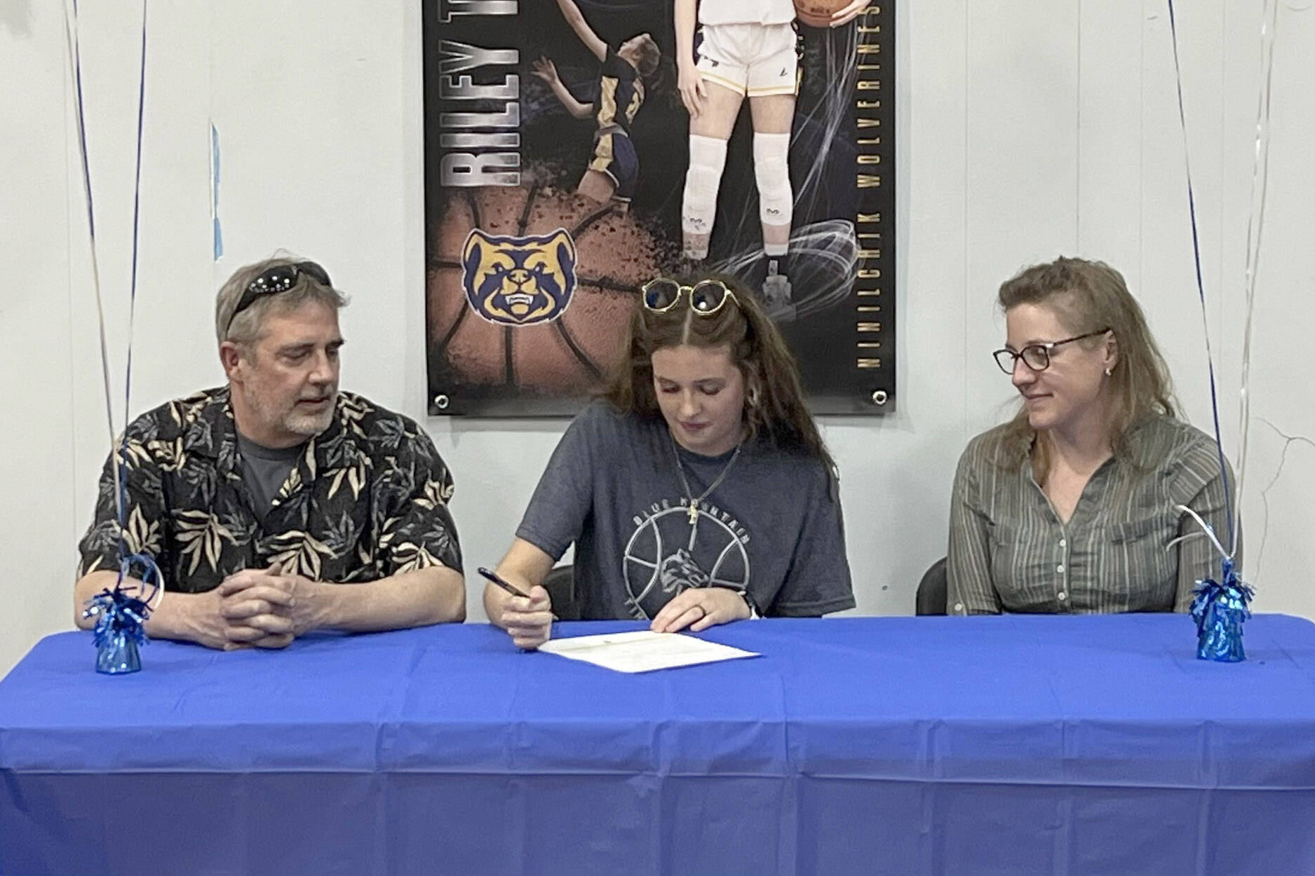 Riley Tucker signs a National Letter of Intent to play basketball at Blue Mountain Community College in Oregon on Monday, April 29, 2024, at Ninilchik School in Ninilchik, Alaska. At left is Riley's father, Tony Tucker, and at right is Riley's mother, Danielle Tucker. (Photo provided)