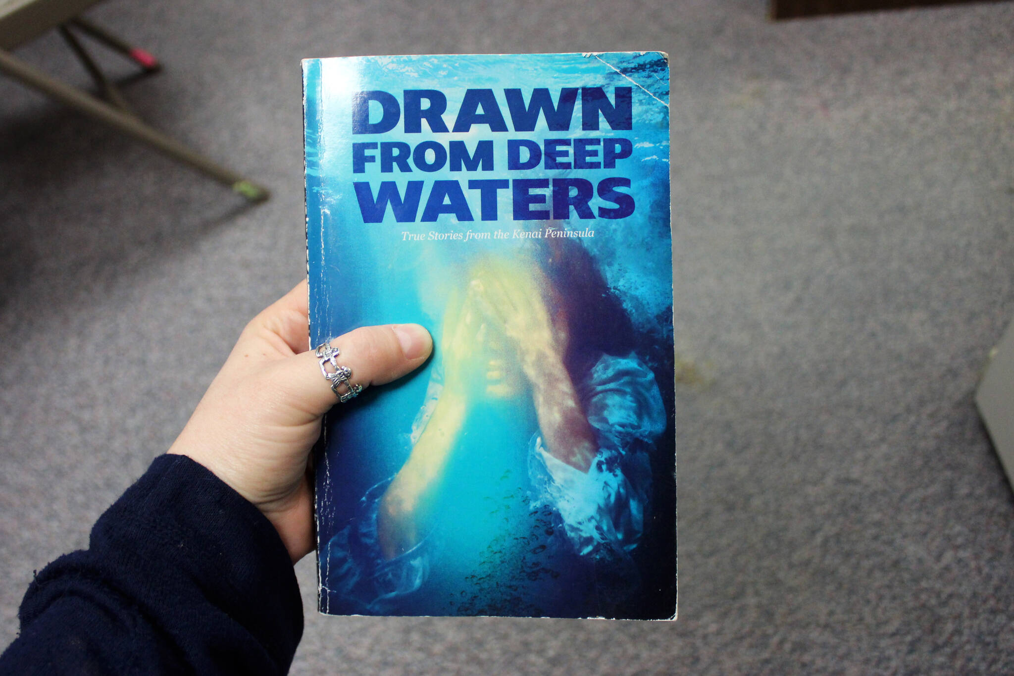 A copy of “Drawn from Deep Waters: True Stories from the Kenai Peninsula,” is held on Thursday, May 9, 2024 in Kenai, Alaska. (Ashlyn O’Hara/Peninsula Clarion)