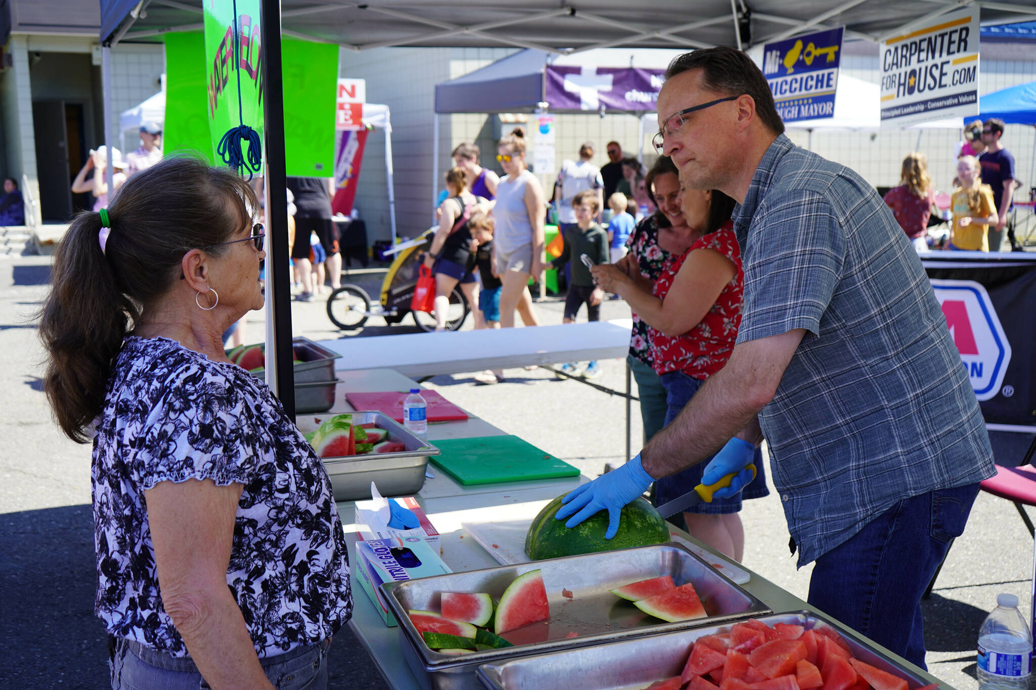 Rep. Ben Carpenter, R-Nikiski, right, slices and serves fresh watermelon during North Peninsula Recreation Service Area’s Family Fun in the Midnight Sun at the Nikiski Community Recreation Center in Nikiski, Alaska, on Saturday, June 15, 2024. (Jake Dye/Peninsula Clarion)