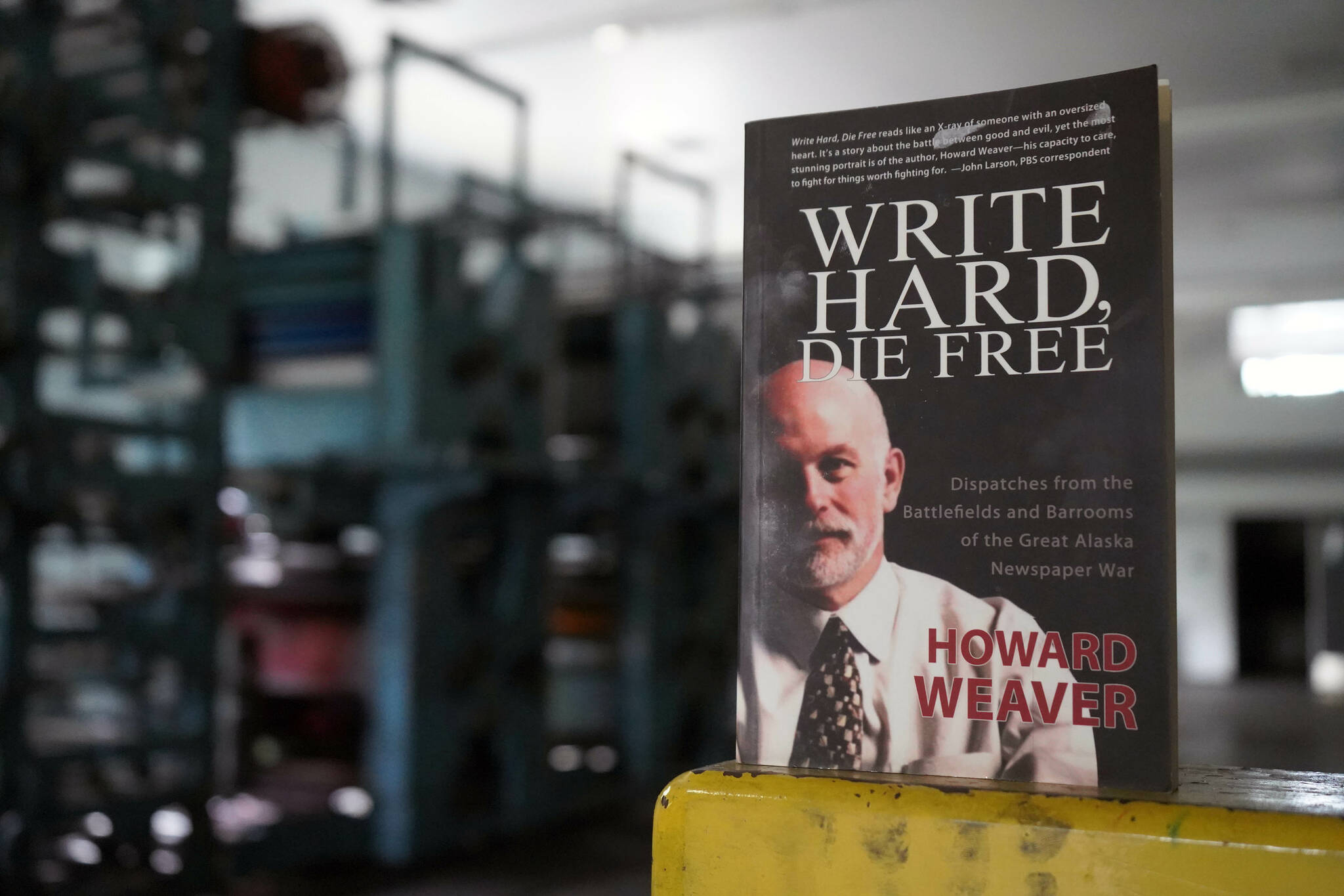 A copy of Howard Weaver’s memoir “Write Hard, Die Free” rests on an ink-splotched guard rail in front of the Peninsula Clarion’s defunct Goss Suburban printing press in Kenai, Alaska, on Thursday, June 20, 2024. (Jake Dye/Peninsula Clarion)