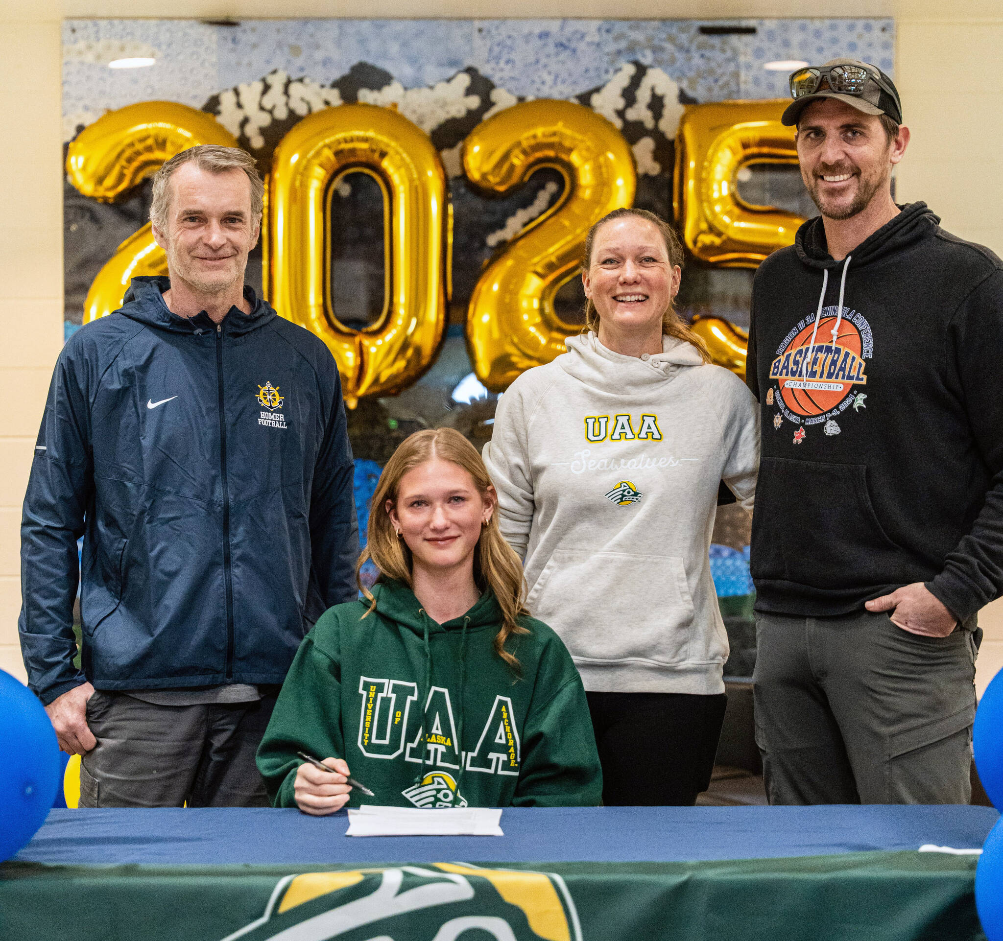 Homer senior Gracie Miotke (seated) committed to run track and field at the University of Alaska Anchorage on Wednesday, March 5, 2025, at Homer High School in Homer, Alaska. Behind Miotke are Homer head coach Bob Ostrom; mother, Amanda Miotke; and father, Dan Miotke. (Photo provided)