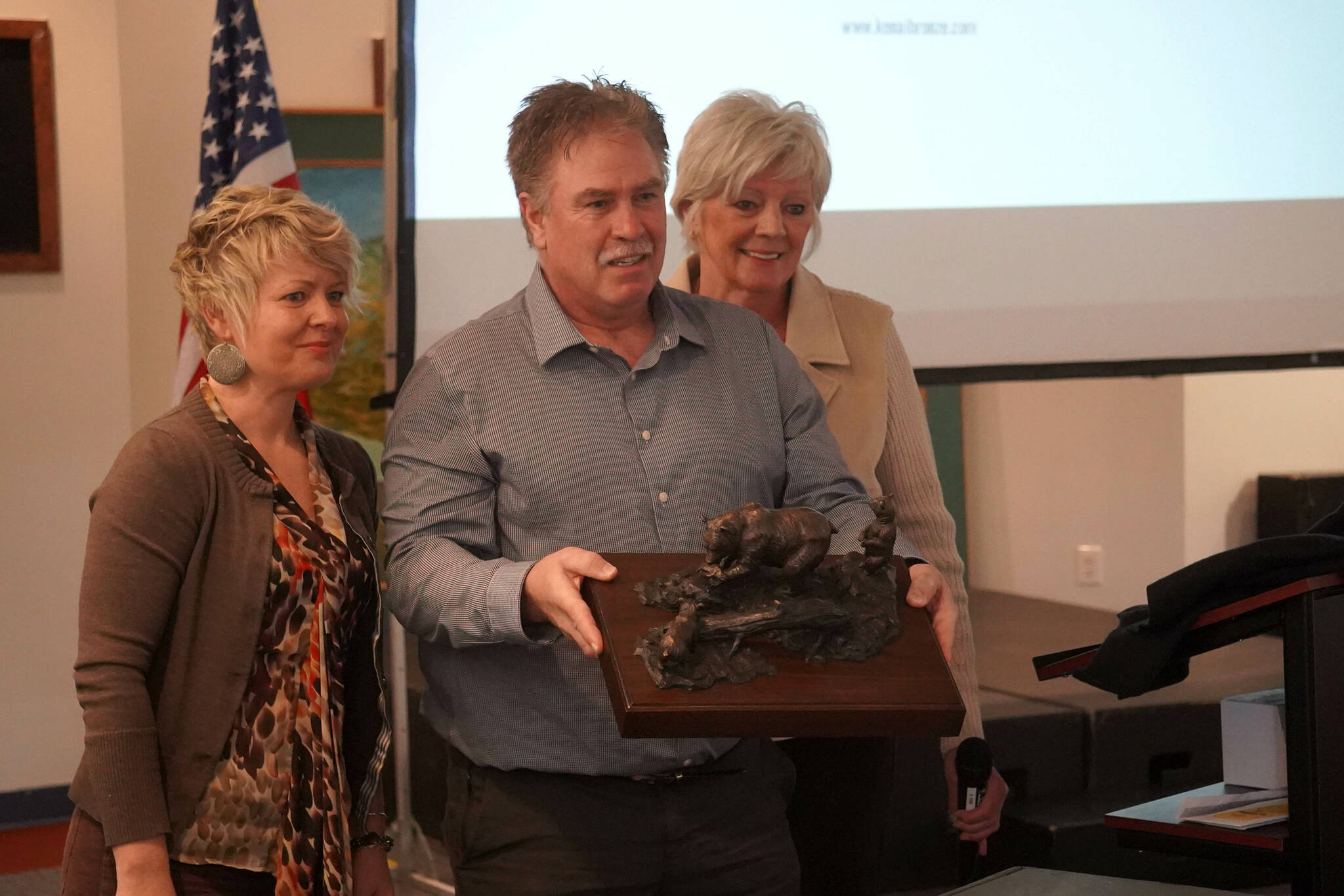 Christine Cunningham, left, and Mary Bondurant, right, both members of the Kenai Bronze Bear Sculpture Working Group, stand for a photo with Kenai Mayor Brian Gabriel and a small model of the proposed sculpture during a luncheon hosted by the Kenai Chamber of Commerce in Kenai, Alaska, on Wednesday, March 19, 2025. (Jake Dye/Peninsula Clarion)
