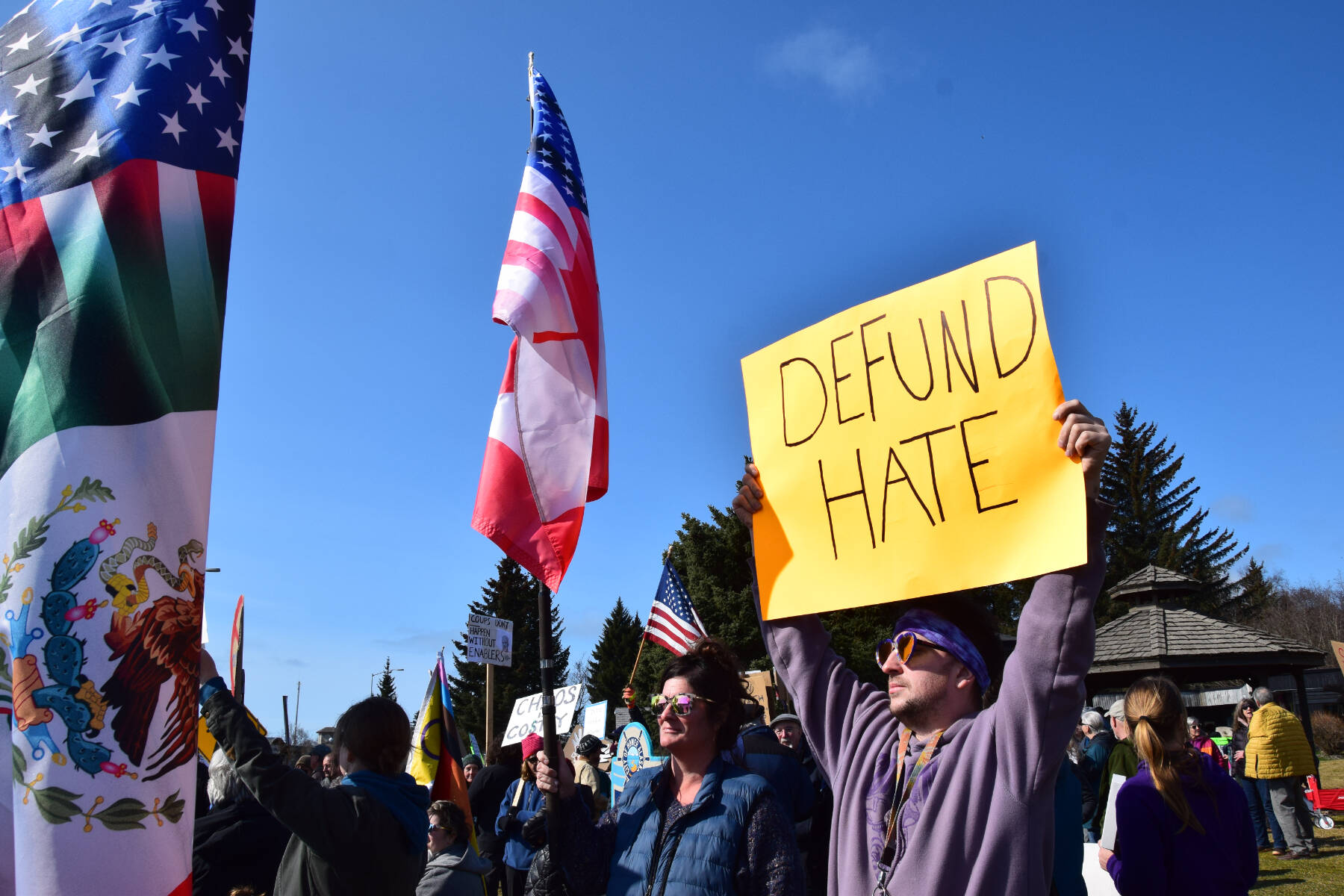 Protestors stand with an American flag and a sign that reads “DEFUND HATE” on Saturday, April 19 at WKFL Park during the “Sustained Resistence, Makes a Difference” Rally. (Chloe Pleznac/Homer News)