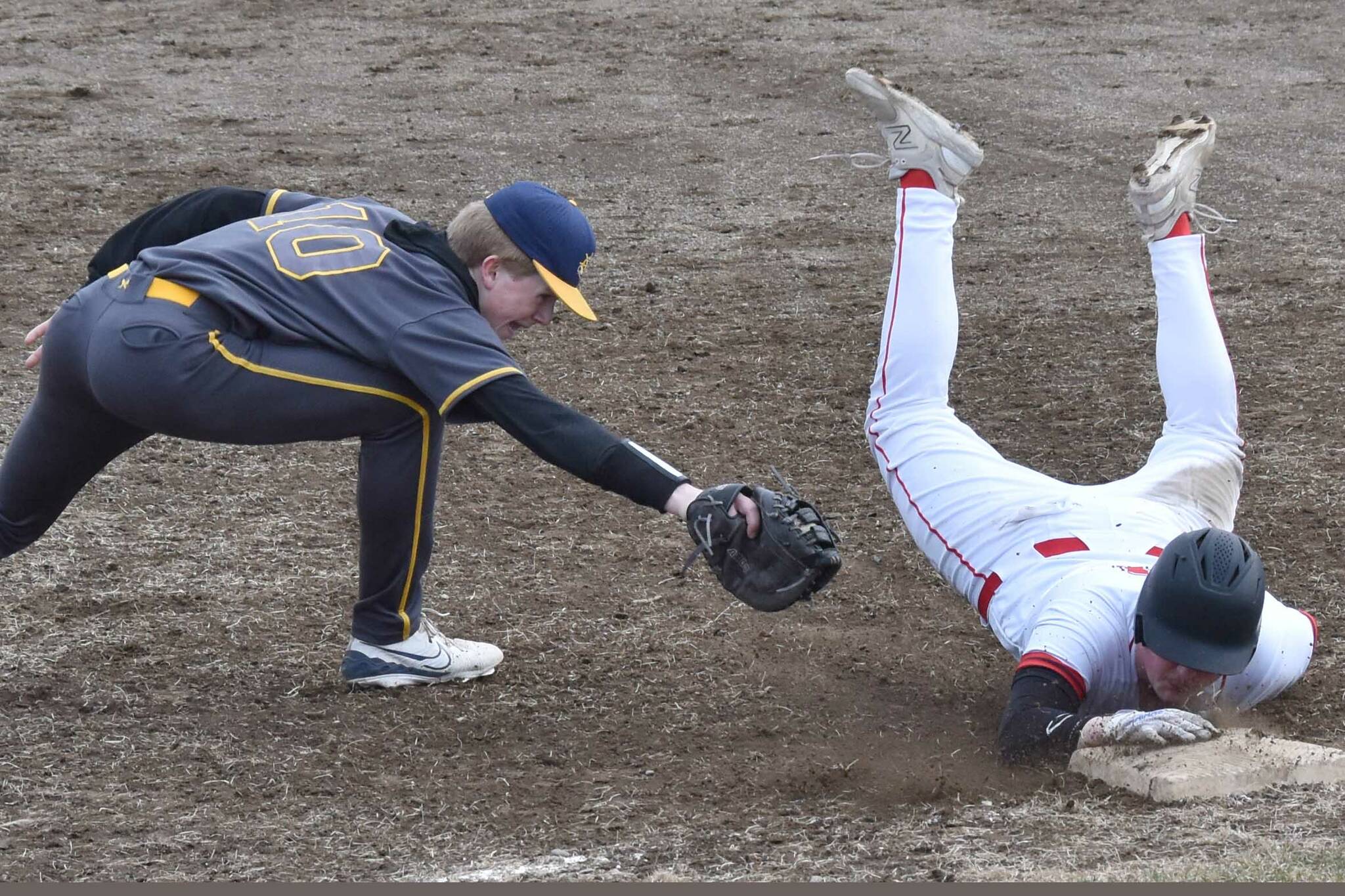 Kenai Central's Gabe Joanis beats the tag of Homer's Henry Wedvik on Friday, April 25, 2025, at the Kenai Little League fields in Kenai, Alaska. (Photo by Jeff Helminiak/Peninsula Clarion)