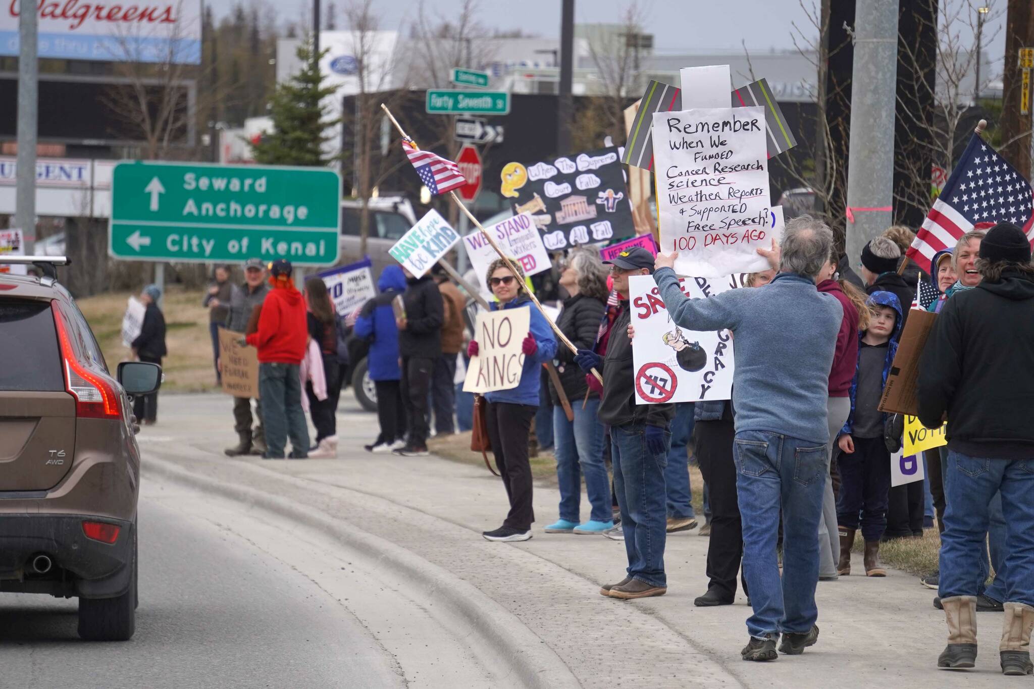 People carry signs and stand as part of a May Day protest alongside the Sterling Highway in Soldotna, Alaska, on Thursday, May 1, 2025. (Jake Dye/Peninsula Clarion)