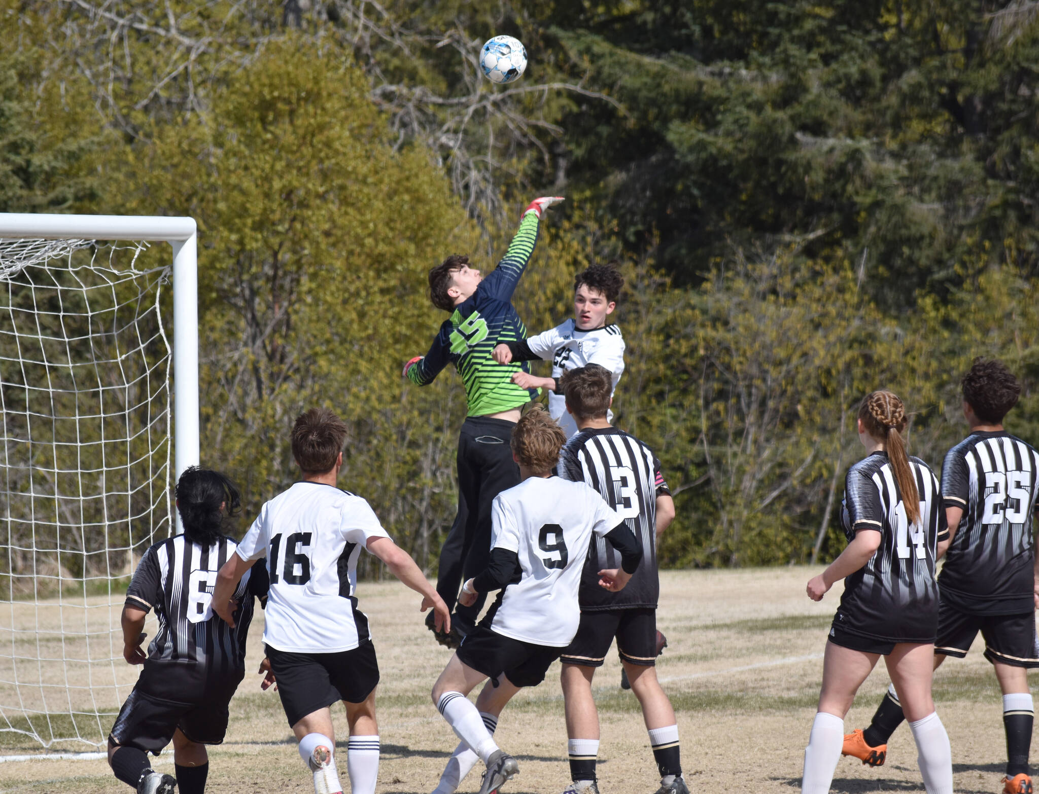 Nikiski goalie Dylan Hall punches the ball away from Kenai Central’s Ben Harris on Friday, May 16, 2025, at Nikiski Middle-High School in Nikiski, Alaska. (Photo by Jeff Helminiak/Peninsula Clarion)
