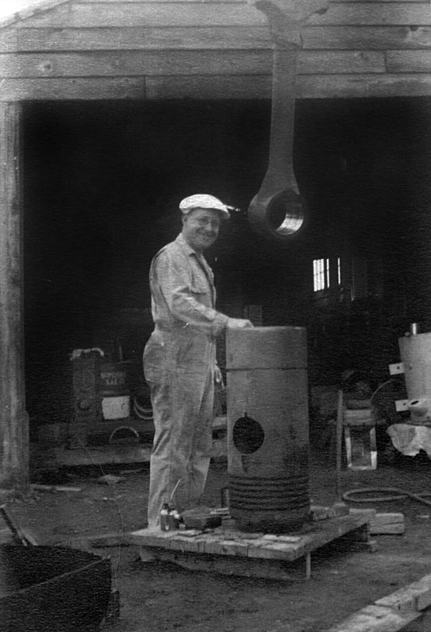 Photo courtesy of the Rowley Family
Frank Rowley smiles as he performs maintenance on one of the four pistons in the large diesel engine that powered the Kenai Power plant. This piston head stands about three feet high and is approximately 18 inches in diameter. Note the size of the connecting rod hanging overhead.