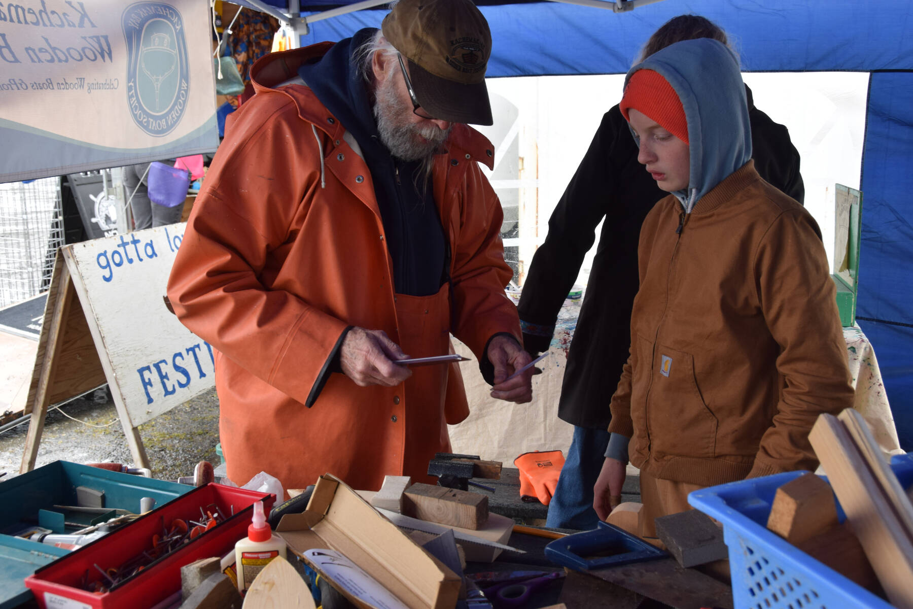 A volunteer from the Kachemak Bay Wooden Boat Society shows a young person how to measure out the wooden blocks needed to construct the perfect, toy wooden boat at the inaugural HomerFest on the Homer Spit on Saturday. (Chloe Pleznac/Homer News)