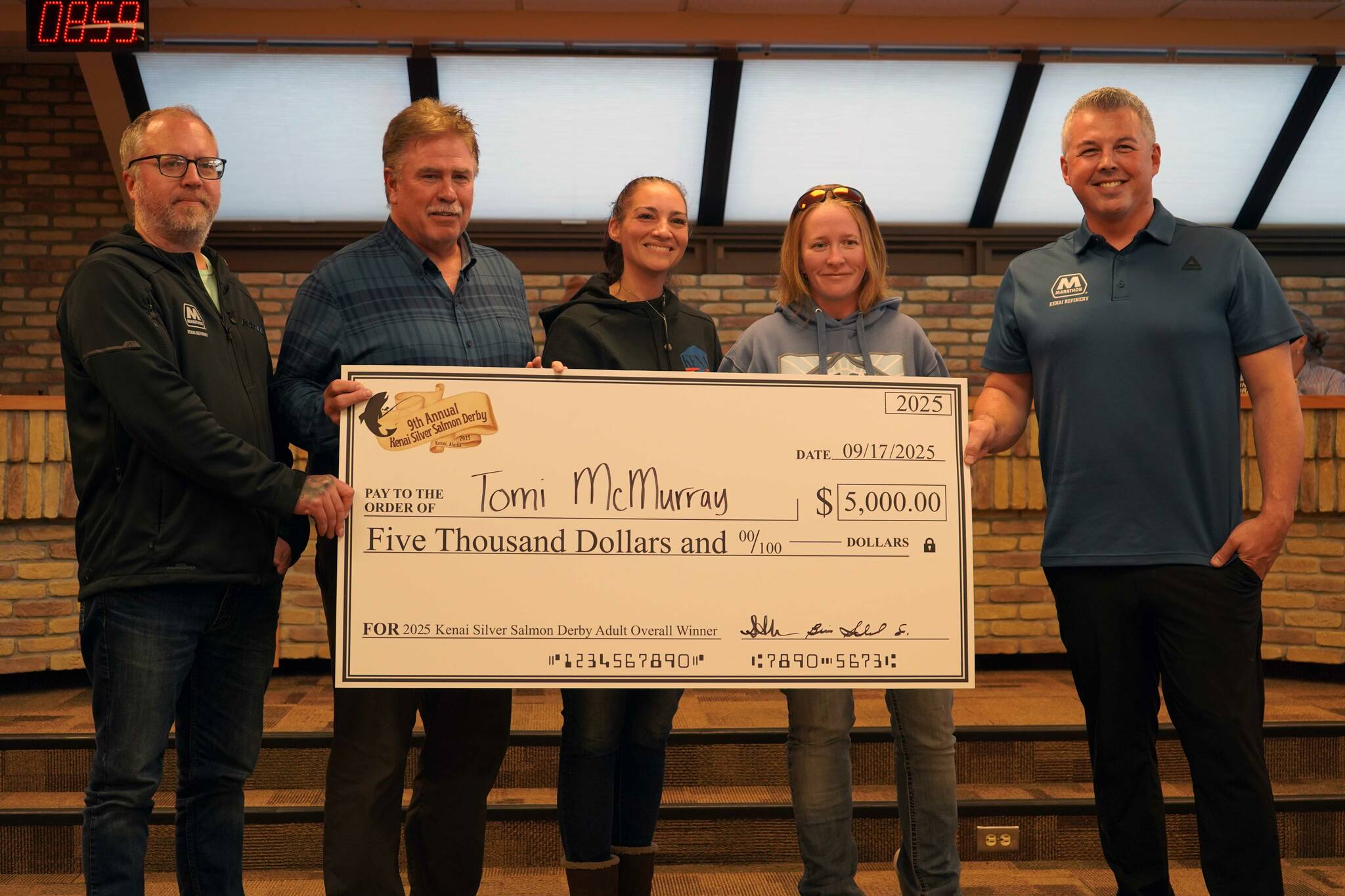 Tomi McMurray, second from right and winner of the Ninth Annual Kenai Silver Salmon Derby, stands with officials from the City of Kenai, Kenai Chamber of Commerce and Marathon Petroleum as shes awarded a novelty check for $5,000 at Kenai City Hall in Kenai, Alaska, on Wednesday, Sept. 17, 2025. (Jake Dye/Peninsula Clarion)