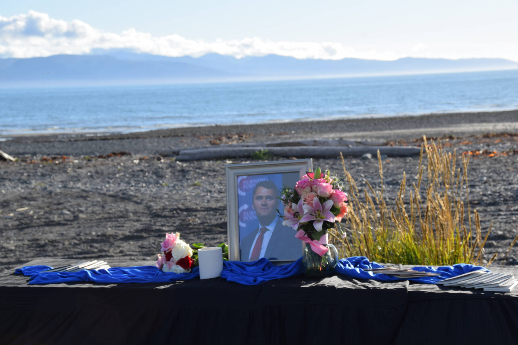 A table, honoring Charlie Kirk, rests on the Homer beach at Mariner Park on Wednesday, Sept. 17, 2025. Copies of pocket constitutions rest beside flowers and an image of Kirk, who was shot and killed in Utah on Sept. 10. (Chloe Pleznac/Homer News)