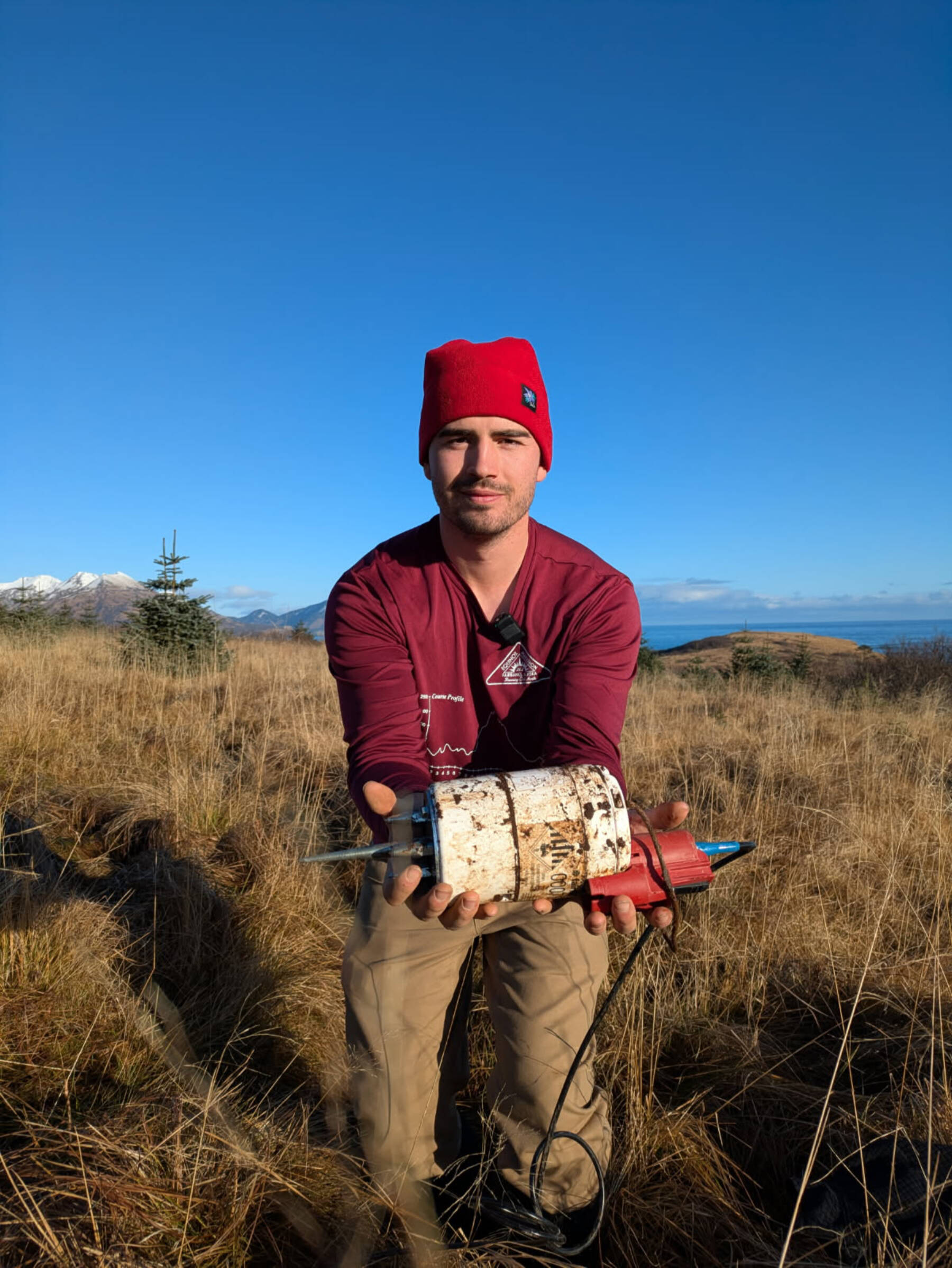 University of Alaska Fairbanks doctoral student Cade Quigley holds a freshly unearthed seismic sensor in Kodiak, Alaska, in November 2025. Photo by Sara Wilbur