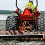 Kenai Parks and Recreation employee Jacob Hart rakes Kenais south beach to demonstrate how the magnetic bar hanging behind his rake picks up nails and other metal debris buried under the sand, on Friday, July 20, 2018 in Kenai, Alaska. The idea of using a magnetic rake to sweep up metal objects  left after many years of pallet bonfires, lost tent stakes, and general litter  came from Kenai Central High School sophmore Riley Graves, who created a magnetic leaf-rake prototype for this Aprils Caring for the Kenai competition. Kenai Public Works Department shop foreman Randy Parrish built the rake after Graves idea, which he presented to the Kenai City Council on May 16. Since the July 10 beginning of this summers personal use dipnet fishery, Hart said the rakes been deployed every evening. When you drive over a dark spot in the sand, where you can tell its been a fire pit, you can hear the nails going tink, tink, tink, he said. (Ben Boettger/Peninsula Clarion)