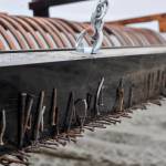 A variety of nails, screws, and staples pulled from the sand of Kenais south beach are stuck to a magnetic bar hanging behind a Kenai Parks and Recreation Department tractor rake on Friday, July 20, 2018 in Kenai, Alaska. Kenai shop foreman Randy Parrish, who built the adjustable chain suspension system, said the magnet can pick up a nail from eight inches away, making it able to pick up nails buried deep in the sand when hung low. (Ben Boettger/Peninsula Clarion)
