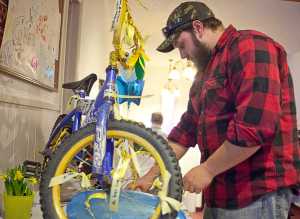 Photo by Rashah McChesney/Peninsula Clarion  Ben Griess hangs a ribbon upon which he wrote "Gone Home" on a bicycle Tuesday Feb. 18, 2014  in the lobby of the  Soldotna Nazarene Church where a memorial for Floyd Murphy was held in Soldotna, Alaska. Murphy Thursday after a swimming accident.