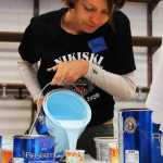 Photo by Kelly Sullivan/ Peninsula Clarion Margy Cox leans over on of the many panels making up the 16-by-28 foot mural community members painted Friday and Saturday, April 11 and 12, at the Nikiski Recreation Center.