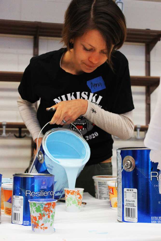 Photo by Kelly Sullivan/ Peninsula Clarion Margy Cox leans over on of the many panels making up the 16-by-28 foot mural community members painted Friday and Saturday, April 11 and 12, at the Nikiski Recreation Center.