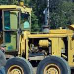 Photo by Rashah McChesney/Peninsula Clarion  Aron Endries, of Endries Construction, guides a motor grader in front of an overturned crane on Beaver Loop Road Wednesday July 30, 2014 in Soldotna, Alaska.  The crane overturned as employees were attempting to move segment of an old culvert being replaced along the road.