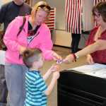 Photo by Dan Balmer/Peninsula Clarion Diane Hinshaw hands a sticker to five-year-old Urijah Walden and his mother Tasha Walden after voting in the primary election at Soldotna City Hall Tuesday.