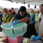 Glen Faulkner, right, and James Slone, center, work the cotton candy machine at the Hilcorp tent while Laura Favretto, left, hands out their wares during Industry Appreciation Day Saturday on the green strip in Kenai.