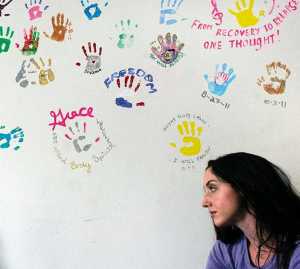 Clarion file photo Kelsey Cusack, volunteer Yoga teacher at the Serenity House treatment center, stands near a wall of handprints made by previous graduates of the substance abuse program. The organization is screening a documentary about addiction on Sunday at the Orca Theater in Soldotna.