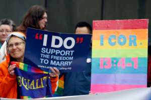 Lin Davis, of Juneau, Alaska, shown wearing an orange rain coat, holds signs supporting gay marriage during a news conference Friday, Oct. 10, 2014, outside the federal courthouse in Anchorage, Alaska. A federal judge on Friday heard arguments from five gay couples seeking to overturn the state's ban on gay marriage. (AP Photo/Mark Thiessen)