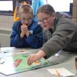 Ben Boettger/Peninsula Clarion Drew Cox looks on as Briley Morton moves a game piece at the Soldotna Winter Games Monopoly tournament at the Soldotna Sports Center on Saturday, Jan. 24.