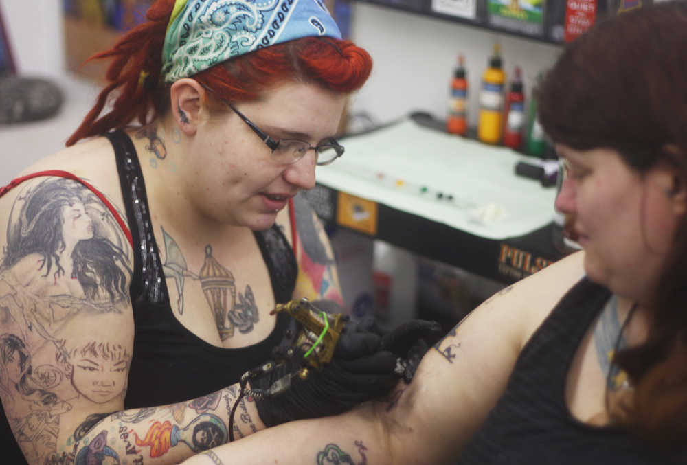 Photo by Kelly Sullivan/ Peninsula Clarion Sam Hayes works on a black and white image of a cat sitting beside a tombstone just below Lori Salyers shoulder, Saturday, March 14, 2015, at Ink Works in Kenai, Alaska.