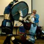 Ben Boettger/Peninsula Clarion Cindy Edmunds (left), known as Dagmar the Red, attacks Jason Notter, known as Hrothi, while Prince Shawn Denny looks on during during the Society for Creative Anachronisms Newcomers Feast at the Soldotna Public Library on Saturday, March 14.