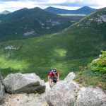 This Aug. 27, 2014 photo shows a hiker climbing up Mount Katahdin with the wilderness of Baxter State Park in Maine in the background. Katahdin is nearly a mile high, the tallest mountain in Maine, and its peak is the northern terminus of the Appalachian Trail. (AP Photo/Beth J. Harpaz)