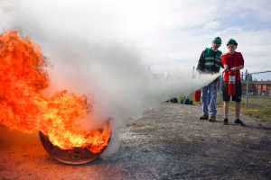 Photo by Rashah McChesney/Peninsula Clarion  John Eller, of Soldotna, helps William Gross, 14, extinguish a fire after a Community Emergency Response Team training drill on Saturday August 8, 2015 at the Soldotna Prep school in Soldotna, Alaska.
