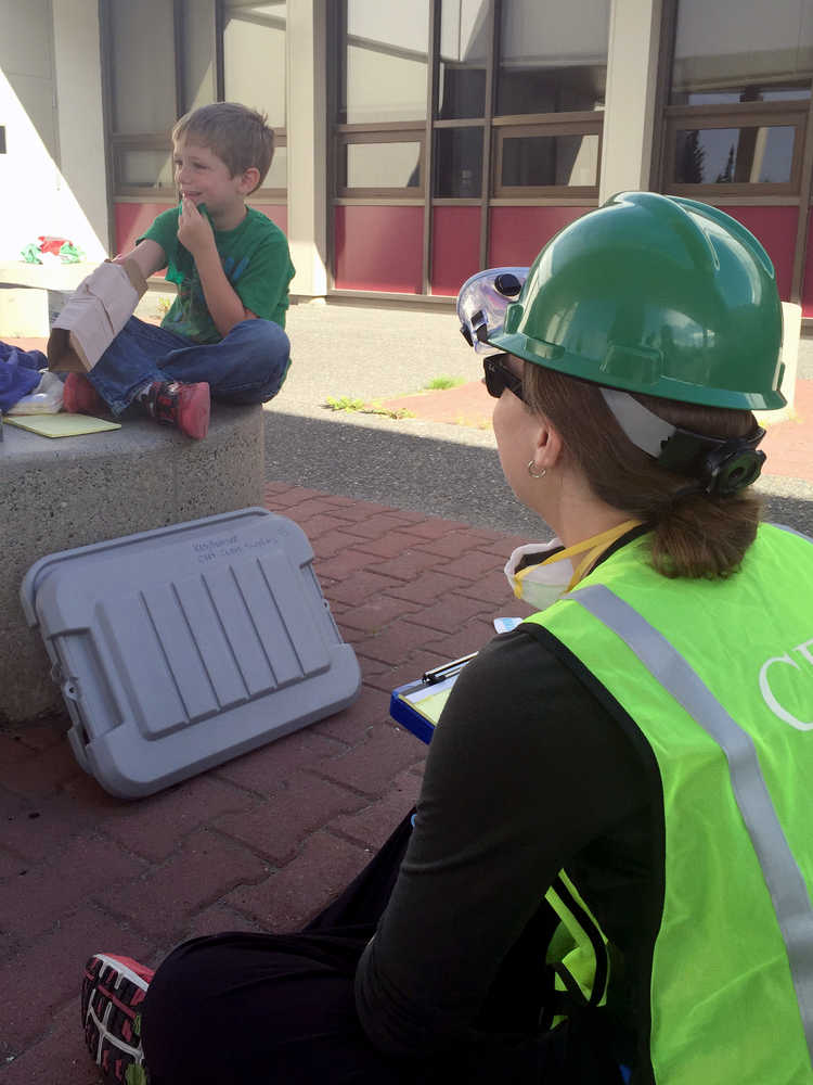 Photo by Megan Pacer/Peninsula Clarion K.J. Hillgren (right) questions 5-year-old Lyman Winger (left) about his fake injuries during an earthquake simulation on Saturday Aug. 8, 2015, at Soldotna Prep School in Soldotna, Alaska. The simulation was the last hurdle for members of this summer's Community Emergency Response Team course.