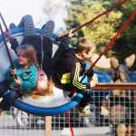 Ben Boettger/Peninsula Clarion Caitlin Cramer (left), Gracee Every, and Carson Cramer ride a circular swing at the dedication of Kenai's municipal park on Saturday, September 12 in Kenai.